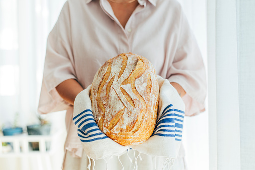 Close-up of fresh baked sourdough bread. Woman is holding wheat and rye beard. She is in kitchen.