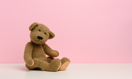 brown teddy bear with patches sits on a white table, pink background, copy space