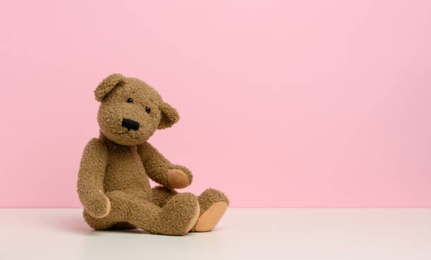 brown teddy bear with patches sits on a white table, pink background brown teddy bear with patches sits on a white table, pink background, copy space doll photos stock pictures, royalty-free photos & images