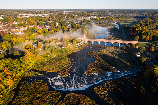 Venta Rapid waterfall, the widest waterfall in Europe and long red brick bridge in sunny, foggy autumn morning, Kuldiga, Latvia. Captured from above