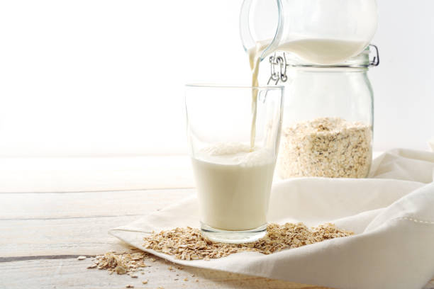 Vegan oat milk is poured into a drinking glass, healthy non dairy alternative on a light wooden table, copy space, selected focus stock photo