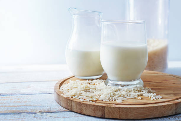 Vegan rice milk, healthy alternative without animal dairy products in a drinking glass and a jug on a wooden kitchen board against a light background, copy space, selected focus stock photo