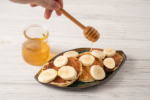 Cheese pancake with banana and honey. Ricotta pancakes with yoghurt and banana. Hand holding honey dipper. High quality photo