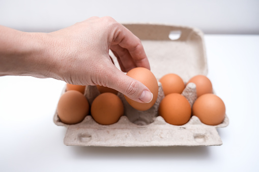 Hand taking one brown chicken egg from a carton box, container for breakfast.