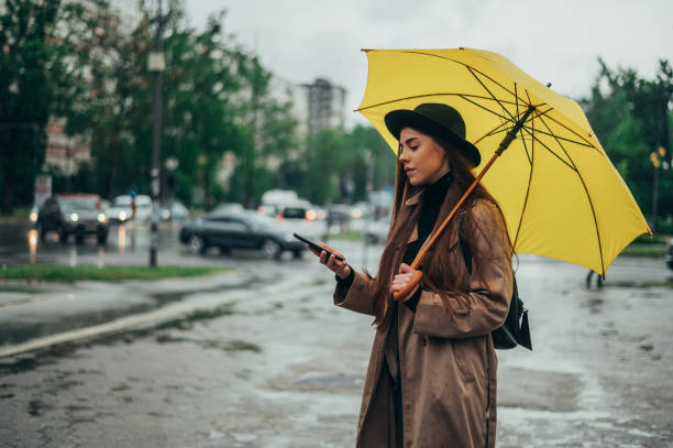 istock Young beautiful woman using smartphone and holding a yellow umbrella 1343648337