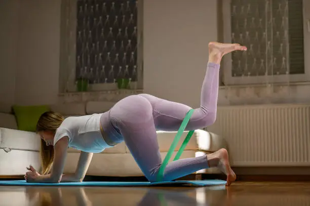 Young attractive woman using resistance band while doing gluteus workout at home