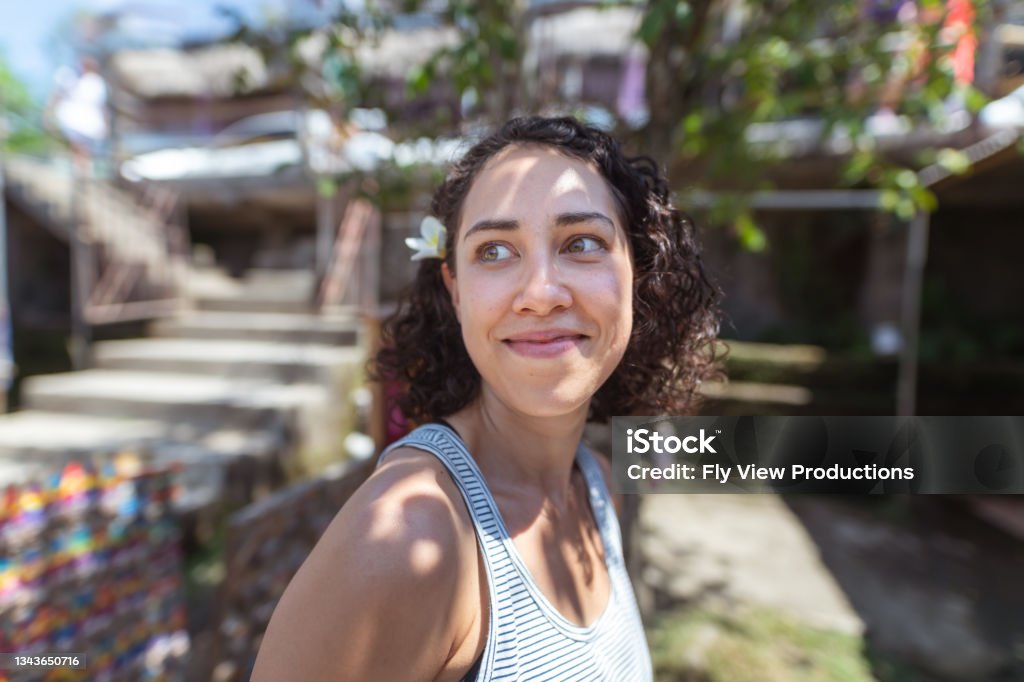 Portrait of mixed race female tourist at outdoor market Portrait of a pretty Eurasian young woman shopping for souvenirs at an outdoor market while on a tropical vacation. The woman has a flower tucked behind her ear. She is looking to the side at something out of frame. Pacific Islanders Stock Photo