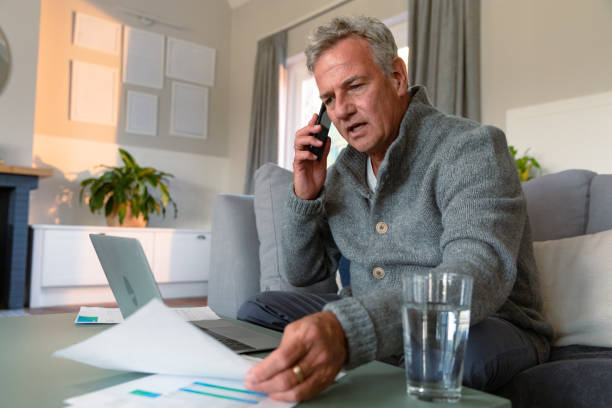 istock Focused caucasian senior man sitting on sofa, doing paperwork, making call and using laptop 1343653451