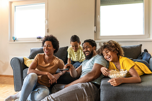 Happy African American family watching a movie and having fun at home on sofa.