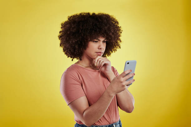 Shot of an attractive young woman using a smartphone and looking unhappy against a yellow background Getting used to a new phone takes a bit of time phone spam photos stock pictures, royalty-free photos & images