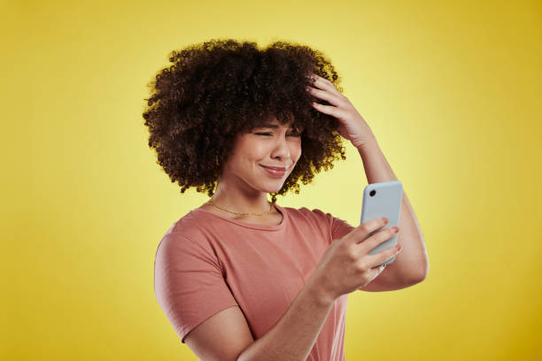 Shot of an attractive young woman using a smartphone and looking unhappy against a yellow background How do you work this thing? phone spam photos stock pictures, royalty-free photos & images