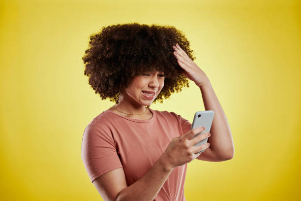 Shot of an attractive young woman using a smartphone and looking unhappy against a yellow background How did this happen? phone spam photos stock pictures, royalty-free photos & images