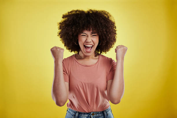 studio shot of an attractive young woman looking excited against a yellow background - extatisch stockfoto's en -beelden