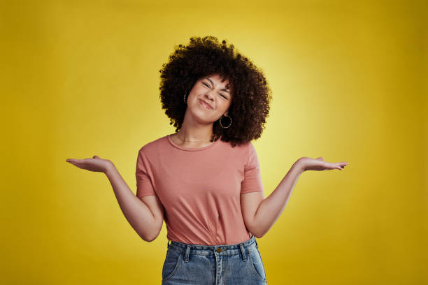 Studio shot of an attractive young woman looking confused against a yellow background stock photo