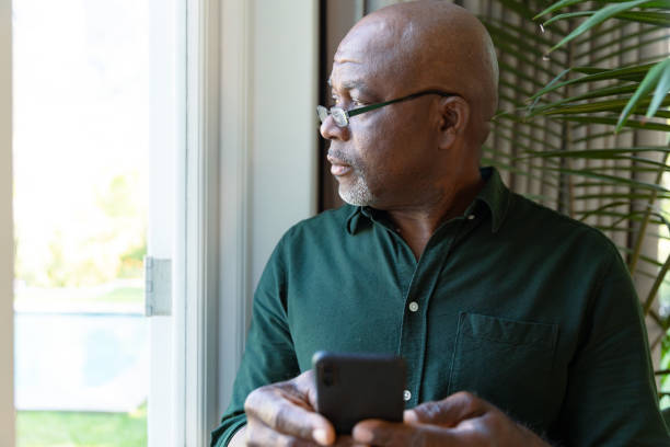 istock Thoughtful african american senior man holding smartphone ale looking outside window 1343672690