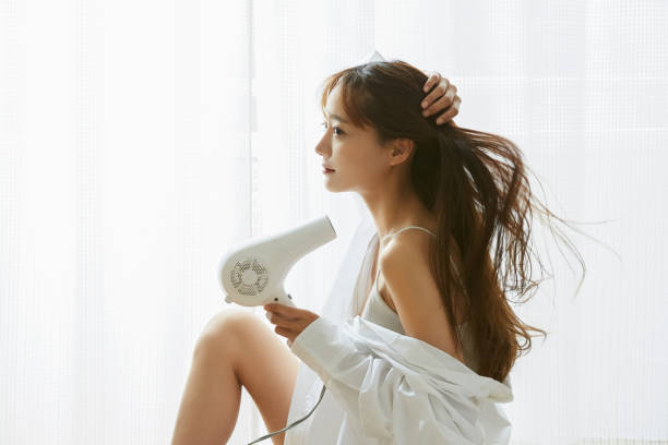 a young asian woman relaxing with a hair dryer - attractive female indoors lifestyles clean imagens e fotografias de stock