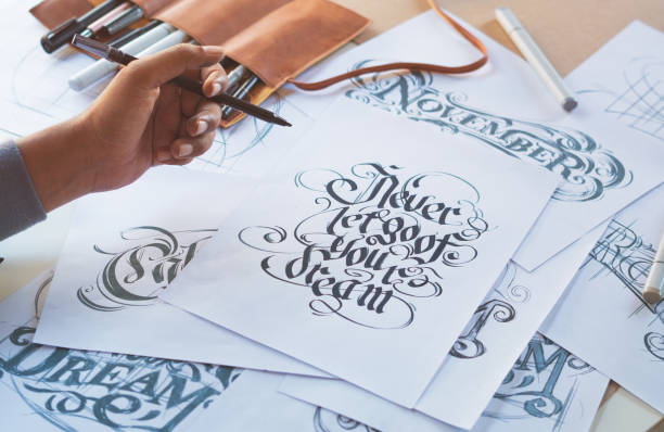 istock Typography Calligraphy artist designer drawing sketch writes letting spelled pen brush ink paper table artwork.Workplace design studio. 1343673530