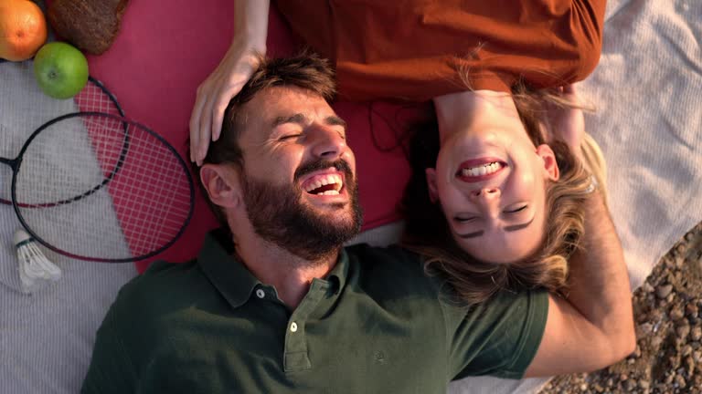 Happy young couple, lying on the picnic blanket, sharing affectionate to each-another, celebrating their love