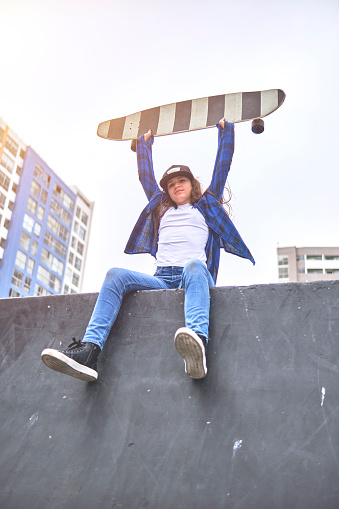 Urban girl having fun riding skateboards at skate park, Portrait of smiling young female skateboarder holding her skateboard. Recreational Activity Concept
