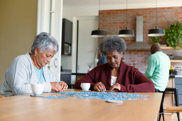 istock Two diverse female friends sitting in kitchen with coffee and doing puzzles 1343679938