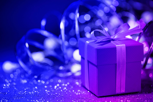 Close-up of a Christmas present (gift box) with defocused christmas lights and decorations in the background. Beautiful lights bokeh.