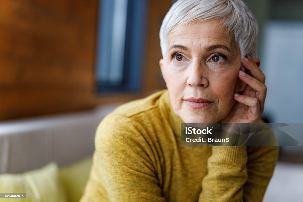 Pensive senior woman with short hair at home. Portrait of a thoughtful mature woman looking away. Senior Women Stock Photo
