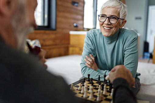 Happy senior woman enjoying while playing chess with her husband at home.