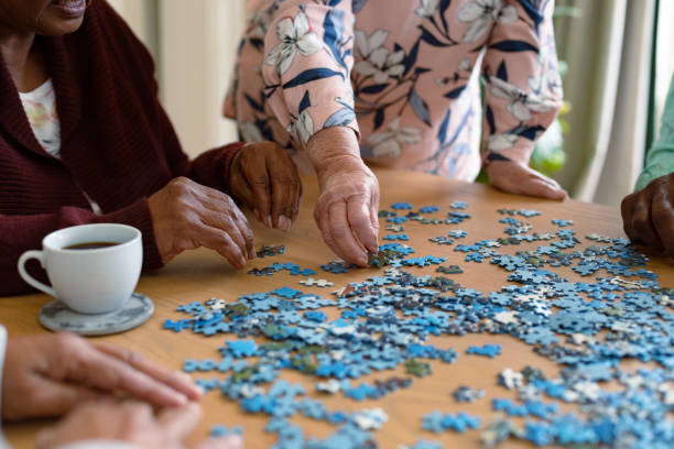 mani di due diverse donne senior e amico maschio afroamericano che fa puzzle - rompicapo foto e immagini stock