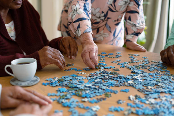 hands of two diverse senior women and african american male friend doing puzzles - puzzel stockfoto's en -beelden