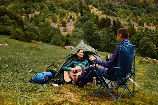Young couple camping by the lake, woman playing guitar