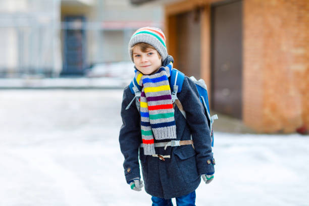 istock Little school kid boy of elementary class walking to school during snowfall. Happy child having fun and playing with first snow. Student with backpack or satchel in colorful winter clothes. 1343714556