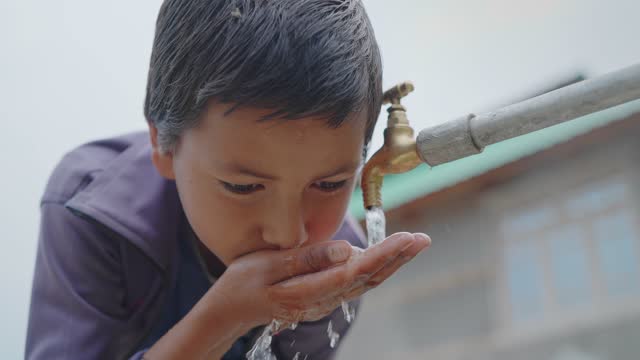 young little boy drinking clean water from a running tap in a rural village.