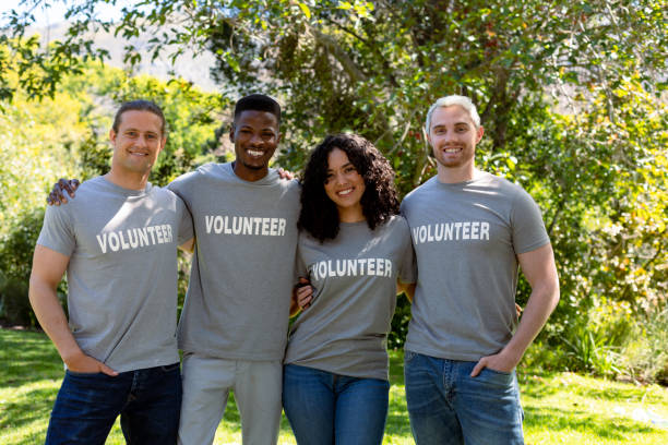 Group of smiling deverse female and male volunteers in matching tshirts looking at camera stock photo