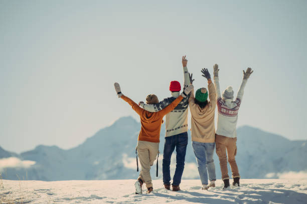 Four happy friends embrace and looks at snow capped mountains stock photo