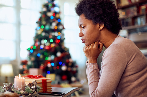 Worried African American woman thinking of something while spending Christmas alone at home.