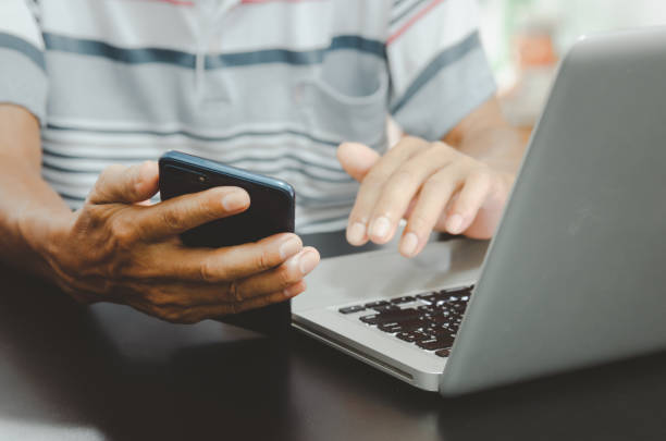 istock man hand using smart phoneand laptop on table at home, searching information  browsing the internet on web, work from home.Business shopping online concept 1343761753