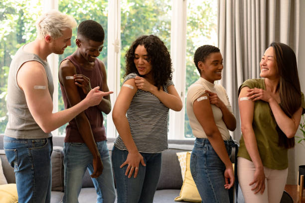 Group of happy diverse female and male friends showing plasters after vaccination stock photo