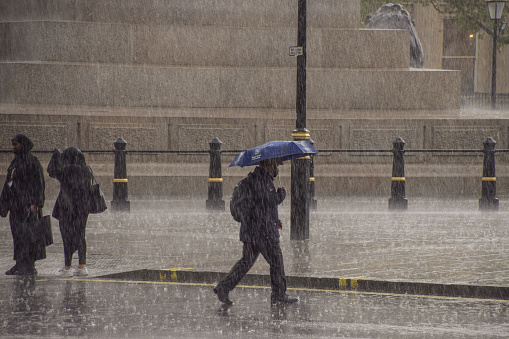 London, United Kingdom -May 18 2021: People with umbrellas in Trafalgar Square as torrential rain falls.