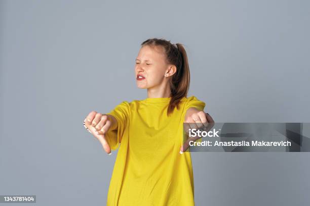 Beautiful Teen Girl With Displeased Face Showing Dislike With Thumbs Down Isolated On Light Gray Background Stock Photo - Download Image Now