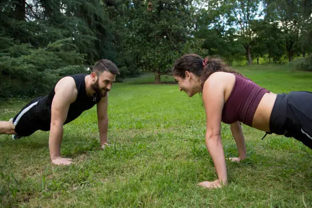 young caucasian man and woman couple practicing sport and push-ups in the park