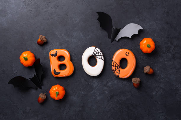 istock Text BOO from gingerbread cookies with decorative pumpkins and bats on dark stone background. Halloween concept 1343788039