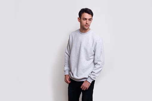 Frontal view of a smiling young brunette man in gray jumper and black jeans isolated white background.
