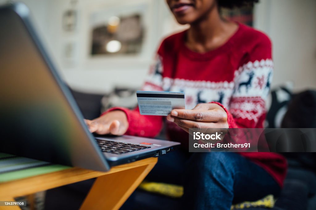 Close up of an unrecognizable African American woman spending winter holidays at home Close up of an unrecognizable African American woman enjoying herself at home during winter holidays, using a laptop to shop online and holding a credit card in her hand Online Shopping Stock Photo