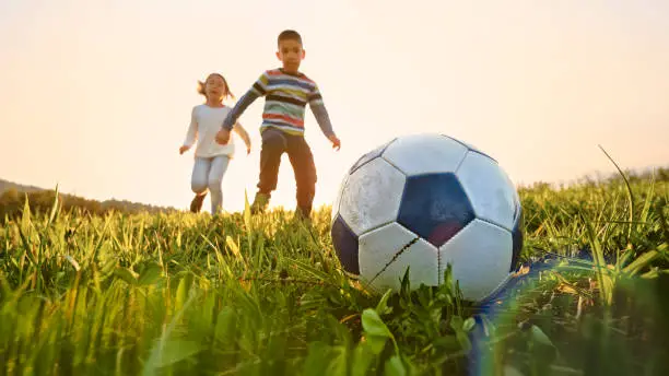 Low angle view of boy and girl playing football on a sunny meadow.