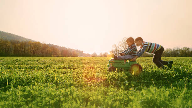 Boy pushing another boy on a toy tractor stock photo