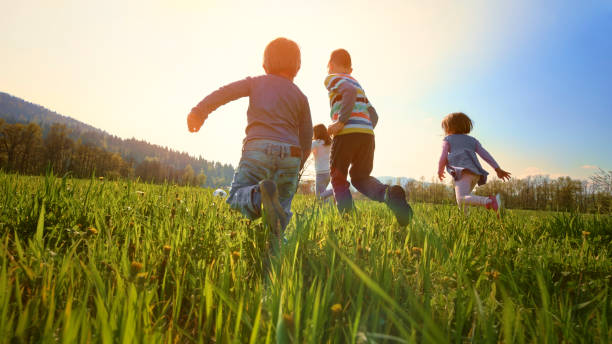 children playing football in a meadow - child rear view running nature imagens e fotografias de stock