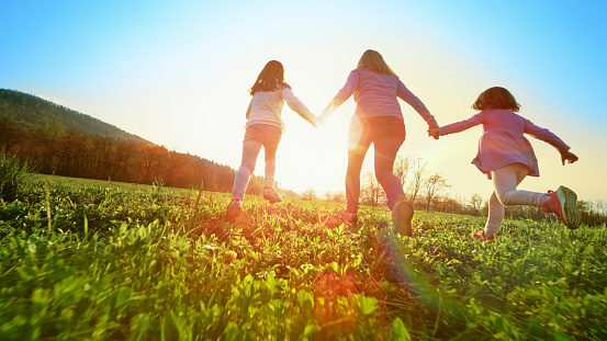 Rear view of girls holding hands while running together in a sunny meadow.