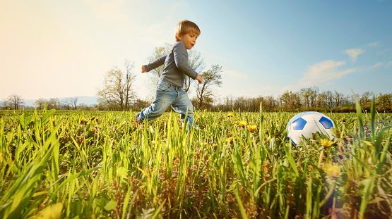 Side view of boy kicking a football in the meadow on a sunny day.