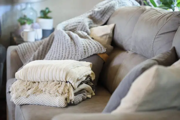 Photo of Stack of a variety of soft knit throw blankets stacked on a grey couch in a farmhouse style living room