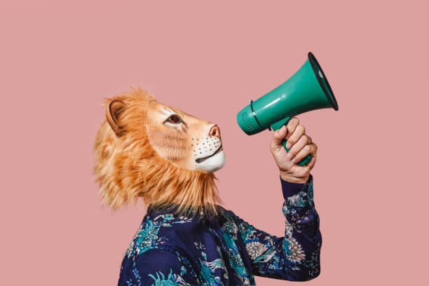 man wearing a lion mask speaks into a megaphone a young man wearing a lion mask speaks into a green megaphone, against a pink background directing photos stock pictures, royalty-free photos & images